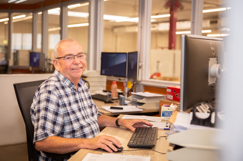 Wim zit achter zijn computer en kijkt ons lachend aan